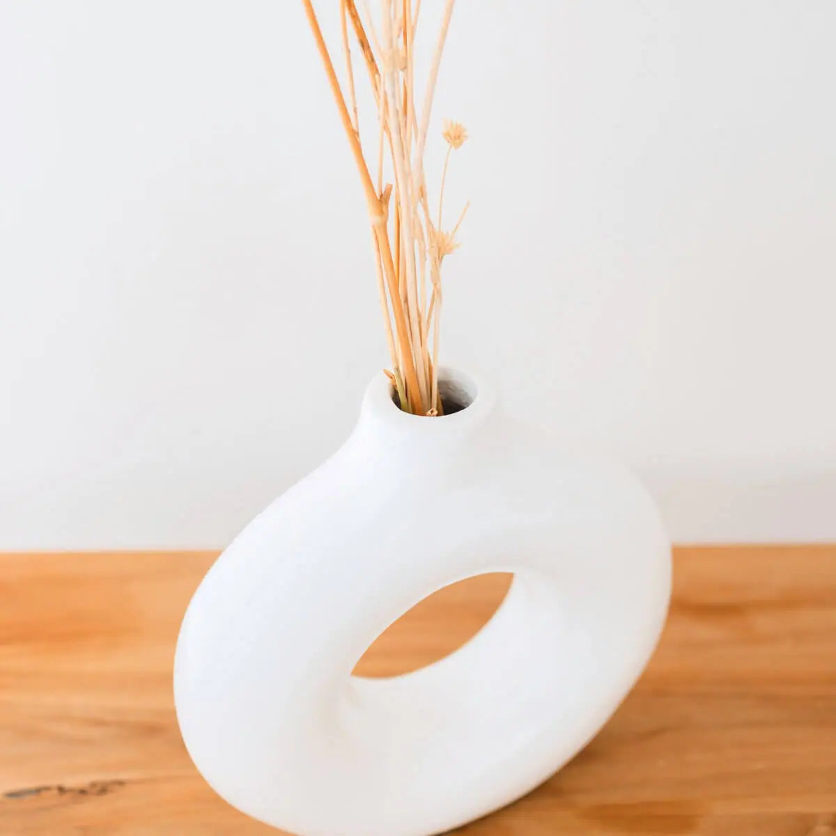 Kleine witte vaas met een droogbloem erin schuin van boven gezien