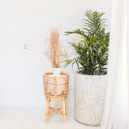 Rotan plantenstandaard met een bloempot er in met een grote stenen bloempot er naast
