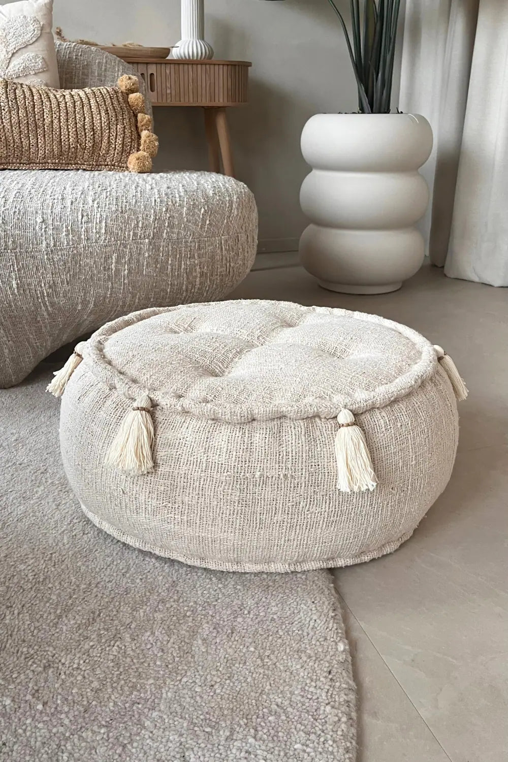 Ronde poef in creme kleur staand op een vloerkleed voor een bank