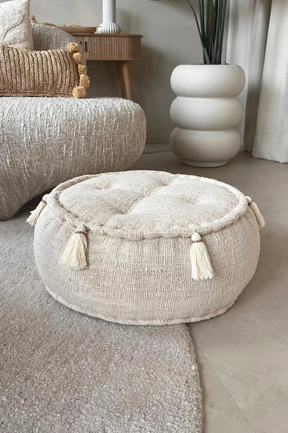 Ronde poef in creme kleur staand op een vloerkleed voor een bank