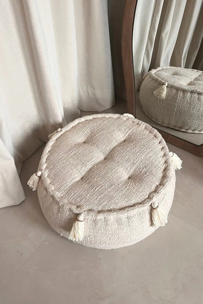 Ronde poef in creme kleur naast een spiegel schuin vanaf boven gezien