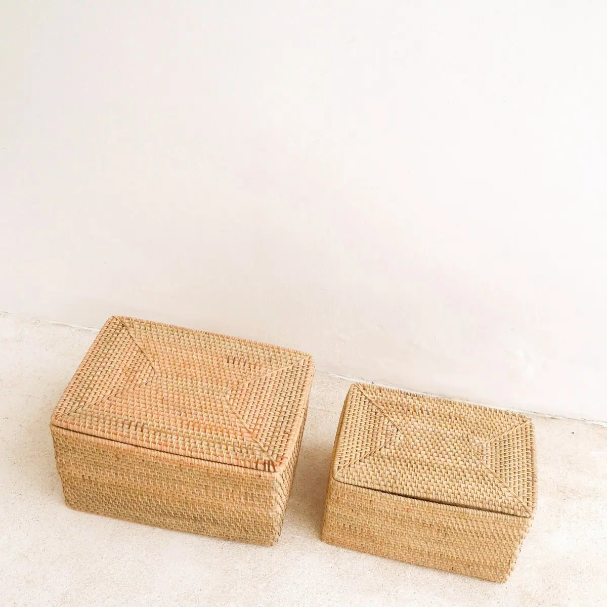 Twee formaten rotan opbergmanden naast elkaar met deksels erop schuin van boven gezien