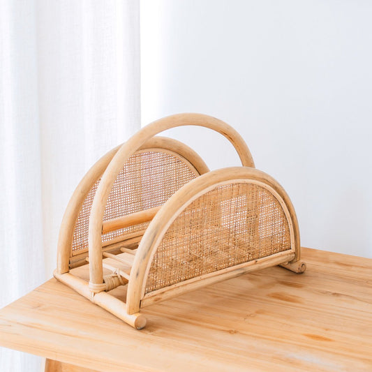 Rotan tijdschriftenmand met twee vakken op een houten tafel, gefotografeerd tegen een witte achtergrond.