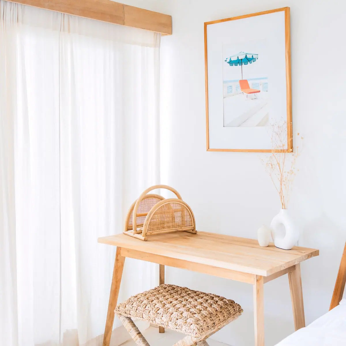 Rotan tijdschriftenmand op een houten bureau in een lichte kamer met witte gordijnen en decoratie op de achtergrond.