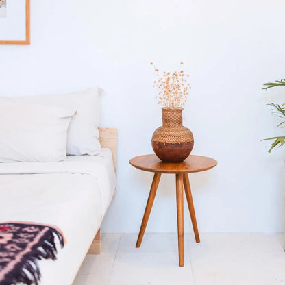 Rotan vaas met hout op een tafeltje naast een bed