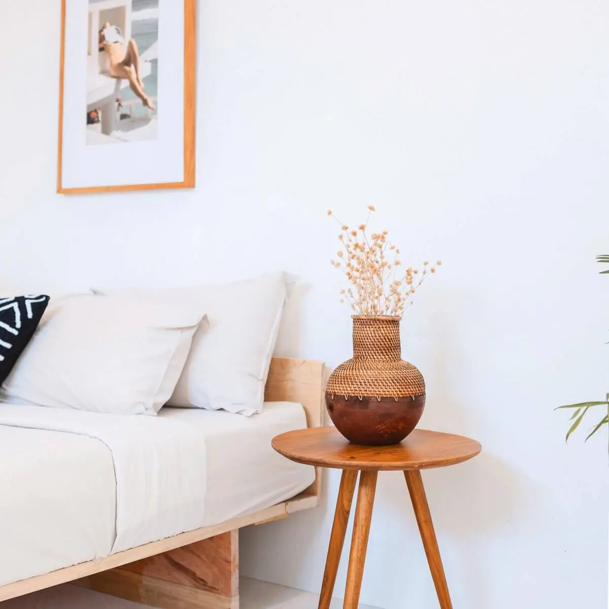 Rotan vaas met hout en bloemen erin op een tafeltje naast een bed