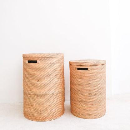 Twee rotan wasmanden met deksel en handvaten naast elkaar staand voor een witte achtergrond