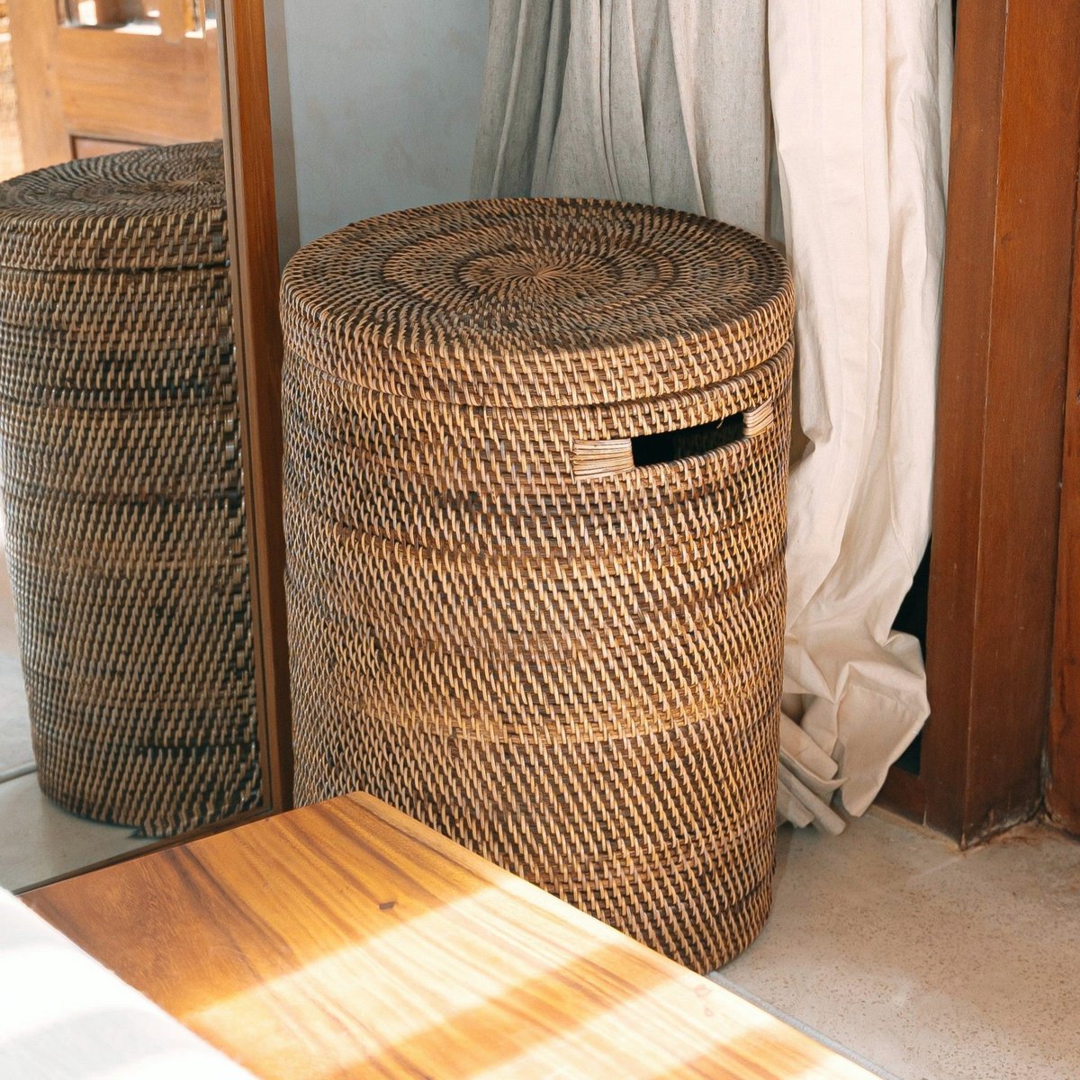 Rotan wasmand met deksel in een lichte kamer bij een houten deur.