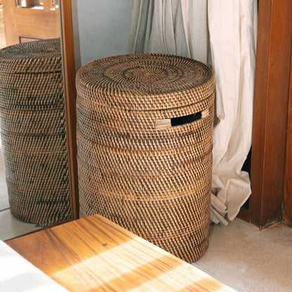 Rotan wasmand met deksel in een lichte kamer bij een houten deur.