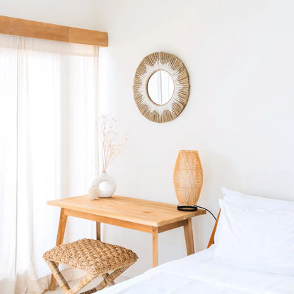 Ronde spiegel van zeegras hangend aan een witte muur boven een tafel