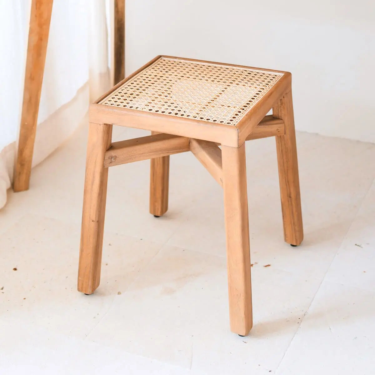 Vierkant houten krukje met rotan zitting staand naast een gordijn