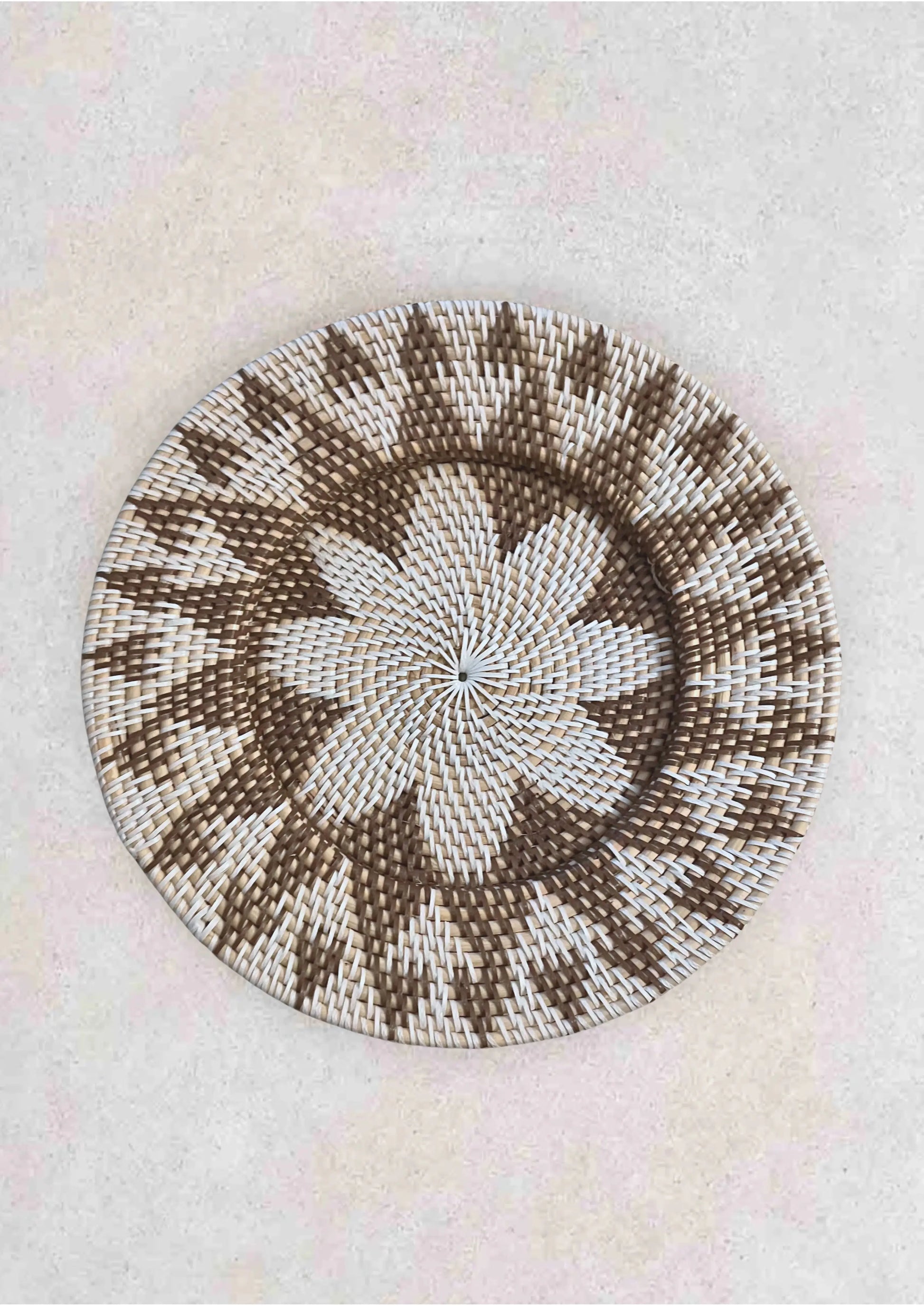 Wandschaal van rotan in de kleuren grijs en bruin op een grijze stenen achtergrond