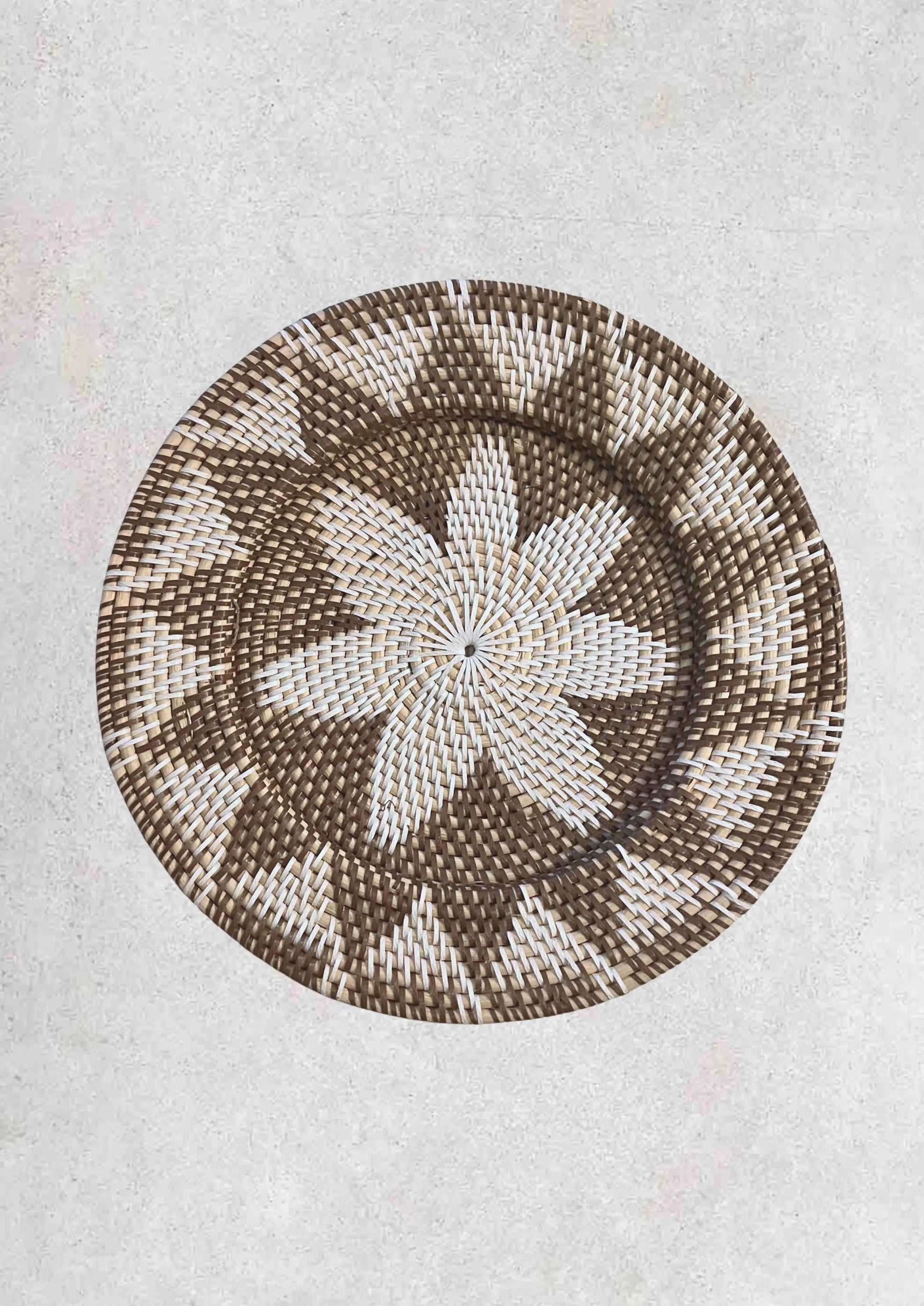 Wandschaal van rotan met een bruin grijs bloempatroon op een lichte stenen achtergrond