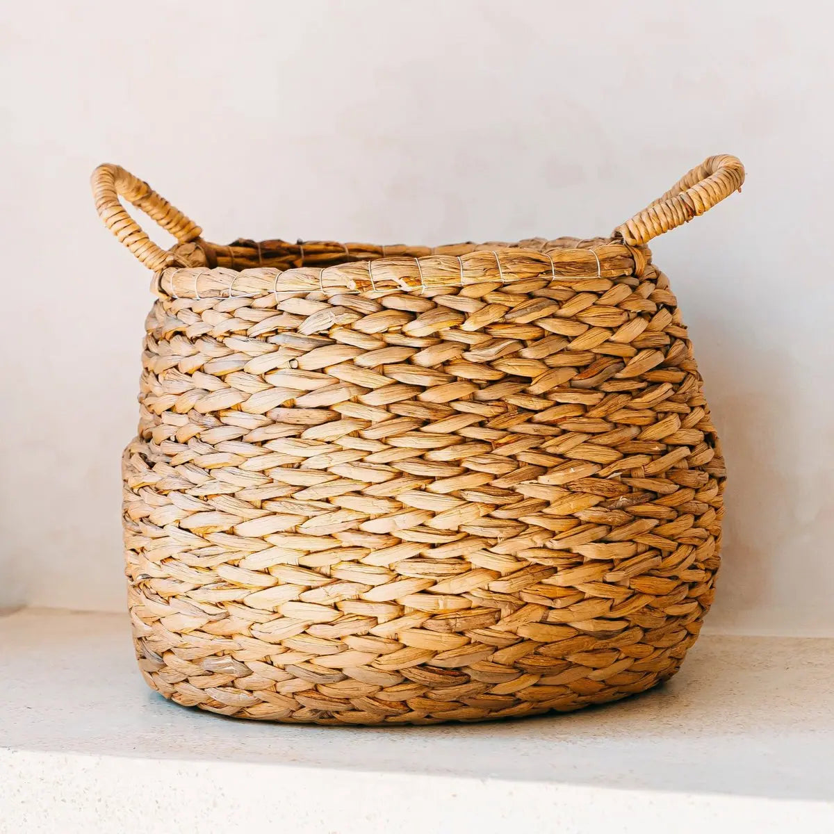 Ronde mand van waterhyacint met handvaten op een beige stenen ondergrond