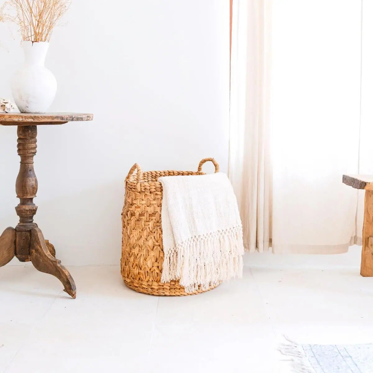 Waterhyacint mand naast een tafel en voor een gordijn met een handdoekje erin